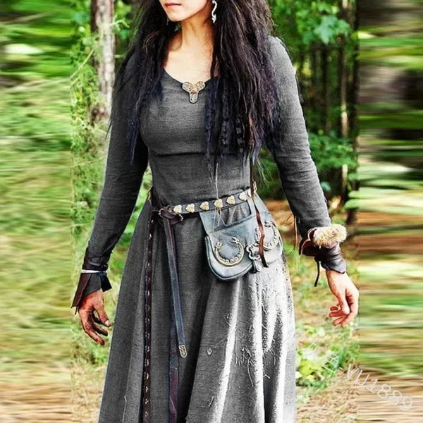 Person in a gray outfit with a belt and pouch standing outdoors.