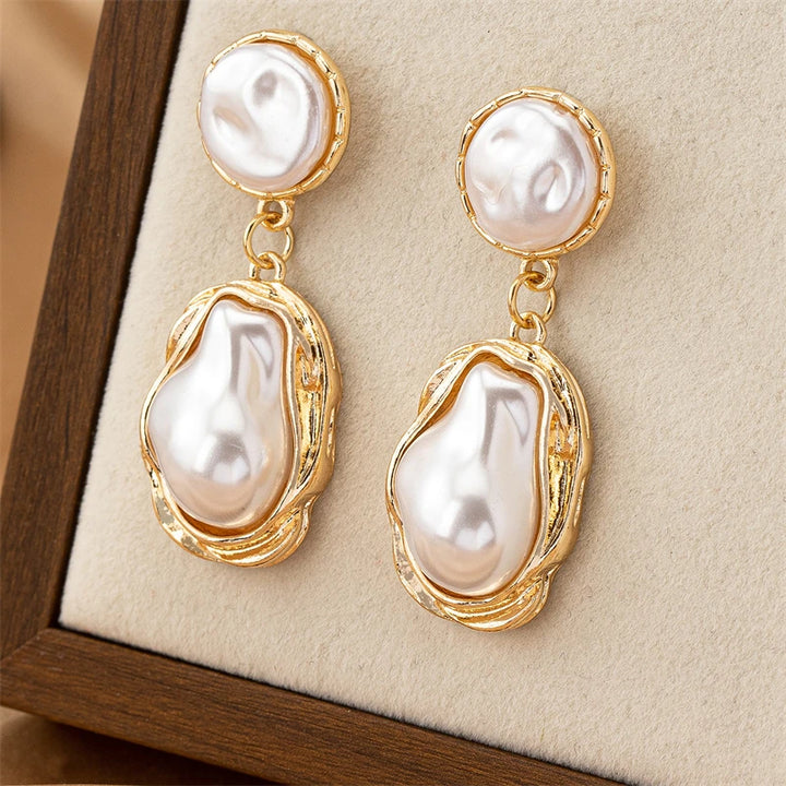 Pearl earrings with gold accents on a beige cushion