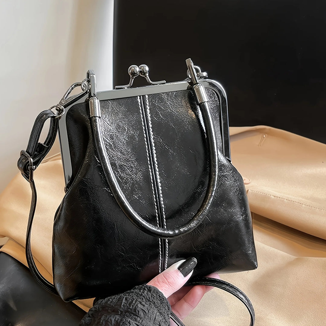 Black leather handbag held by a person with beige pants and black shoes.