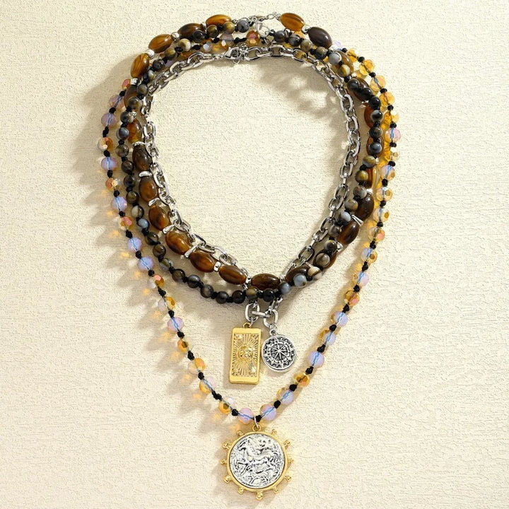 Beaded multi-strand necklace with dark beads and gold accents; square and coin charms pendant