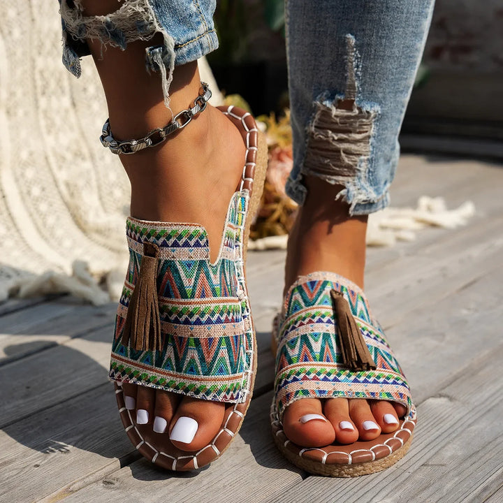 Colorful patterned sandals worn with ripped jeans on a wooden surface.