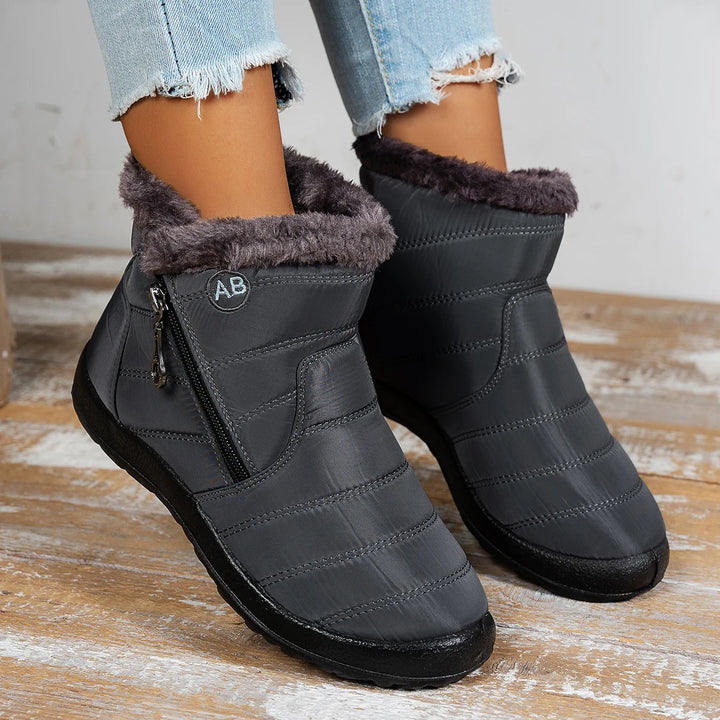 Gray ankle boots with fur lining worn by a person on a wooden floor.