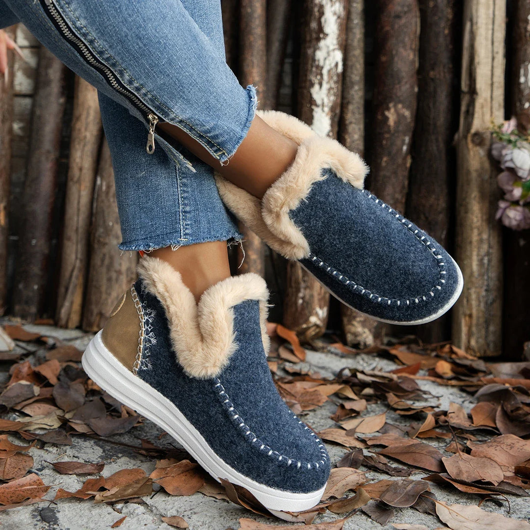 Navy blue boots with beige fur trim worn by a person on a wooden background