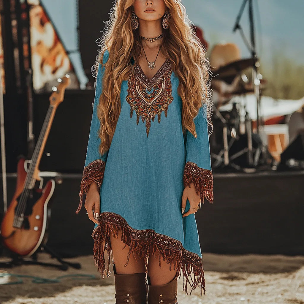 Woman in a blue dress with fringe details standing in front of musical instruments.