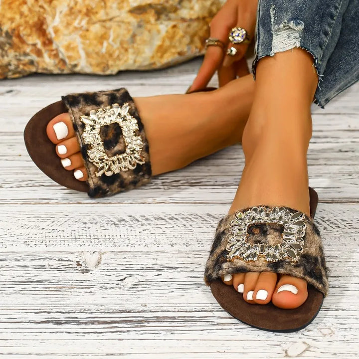 Leopard print sandals with embellishments on a wooden floor.