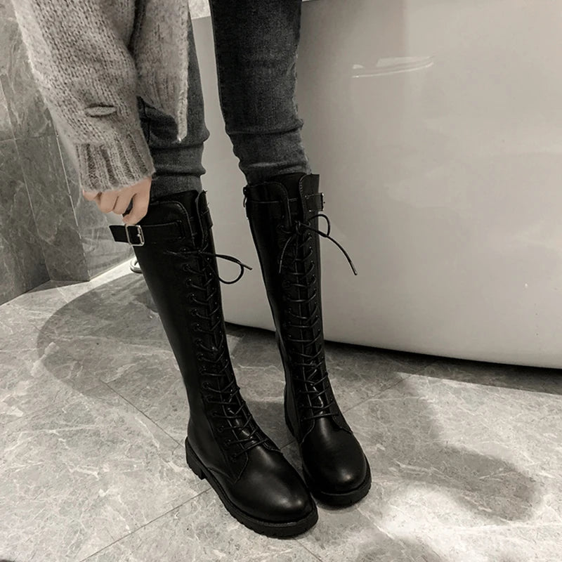 Person wearing black knee-high boots with a neutral background