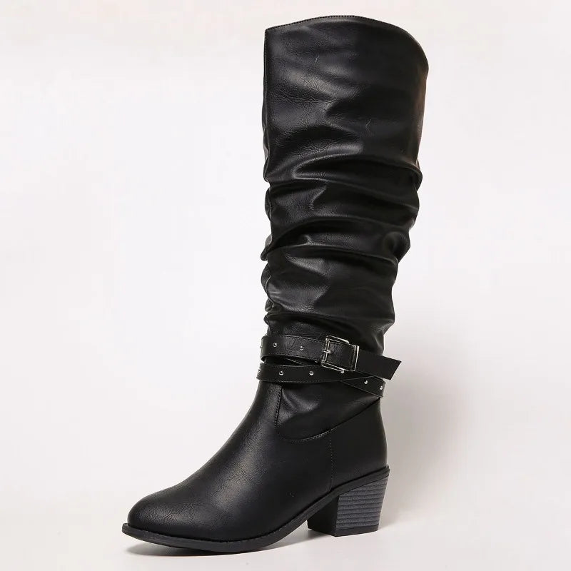 A single black knee-high slouch boot with a low block heel and a decorative strap with silver studs and a buckle around the ankle, shown against a plain white background.