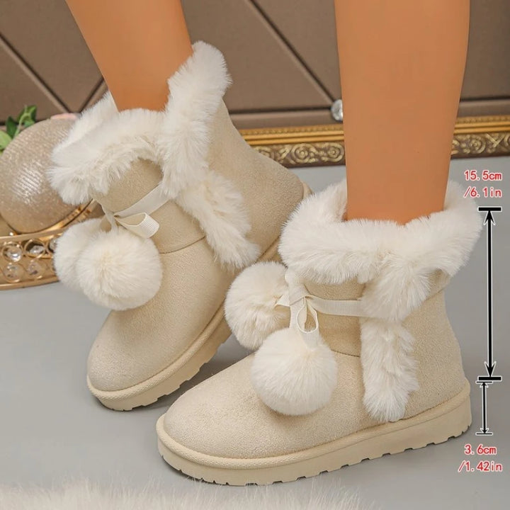 A pair of beige faux-leather ankle boots with fluffy white faux-fur trim, white ribbon bows, and large white pom-poms, shown on a model's feet with a height measurement overlay.
