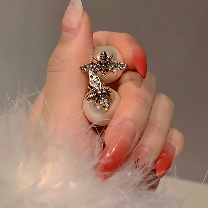 Hand wearing a decorative ring with a bee design on a neutral background