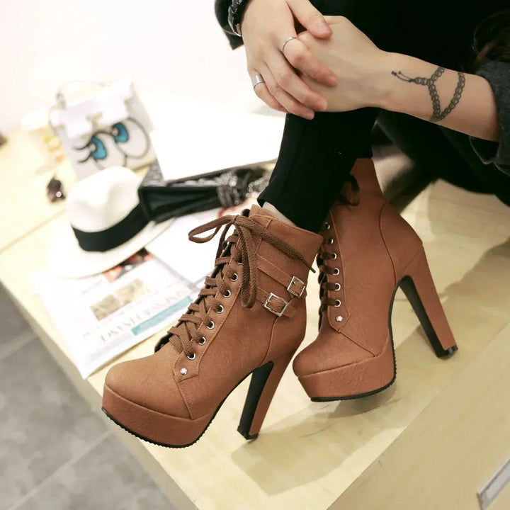 Brown high-heeled platform boots worn by a person sitting on a bench.