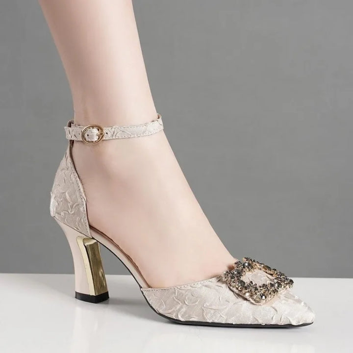 Silver high-heeled shoe with decorative buckle on a gray background