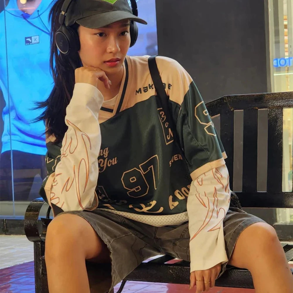 Person wearing a green and beige jacket with '97' on it, sitting on a bench.