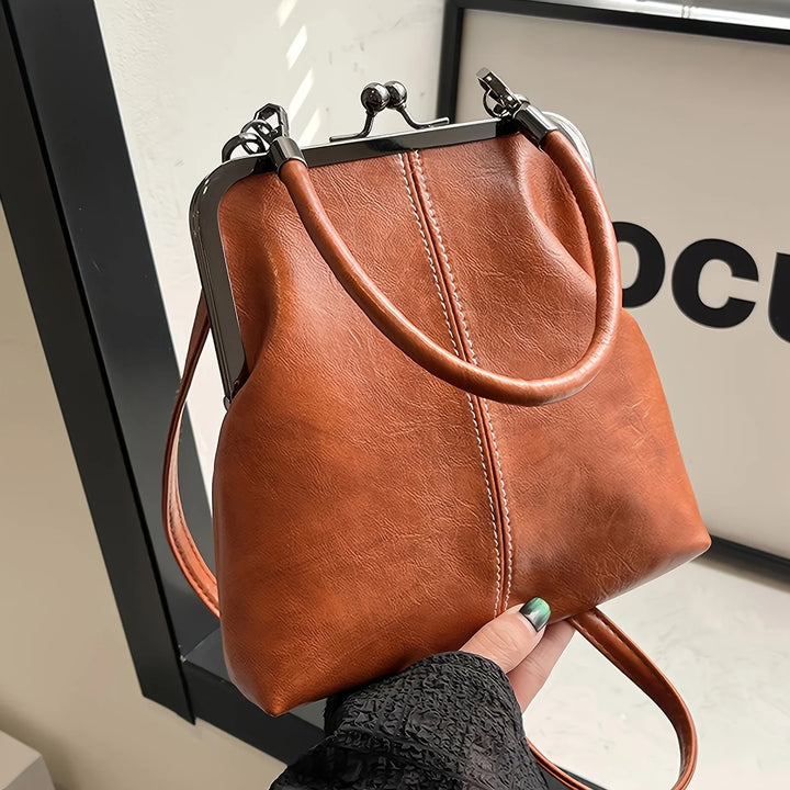 Brown leather handbag held by a person with a blurred background