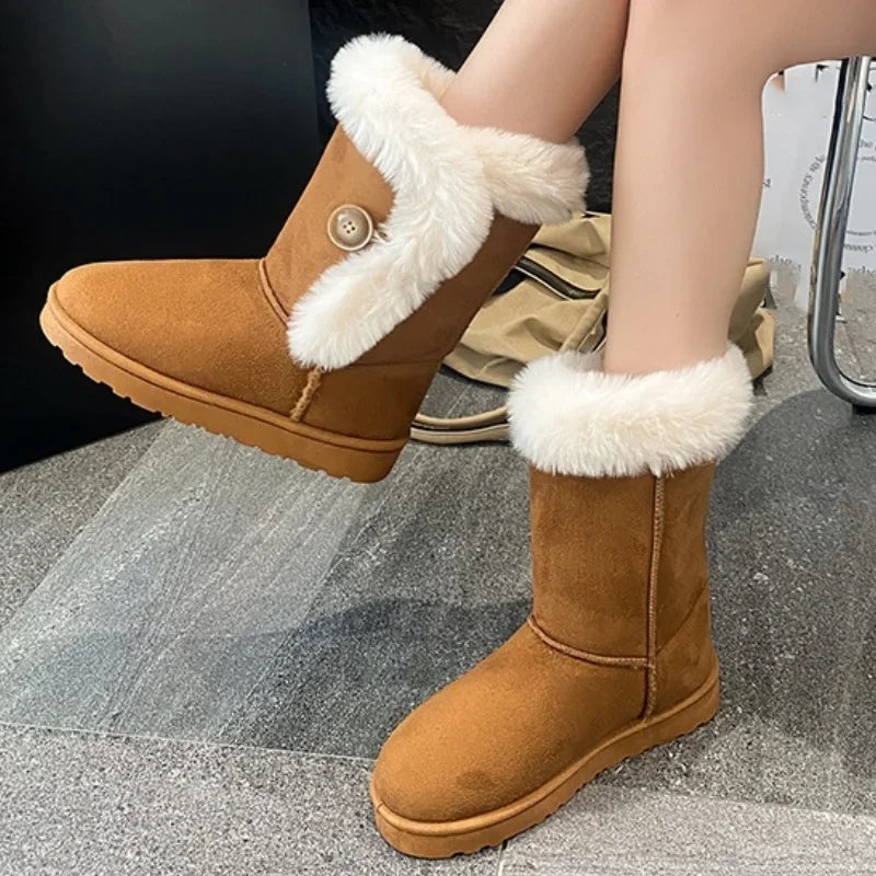 A pair of mid-calf brown suede boots with white faux-fur trim and a decorative button detail, shown on a person's feet against a gray tiled floor background.
