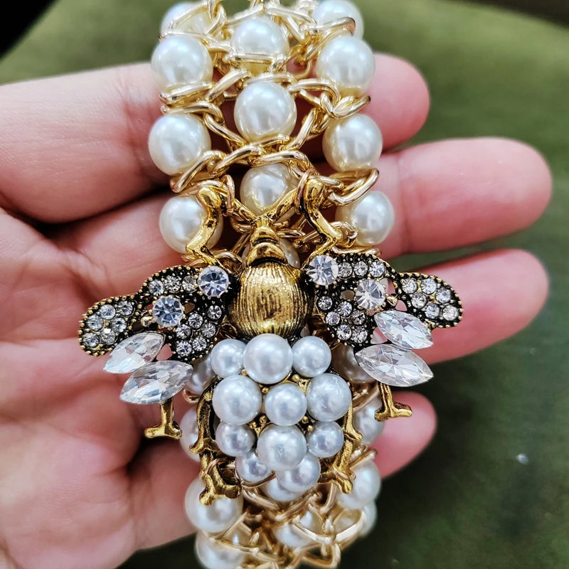 Decorative brooch with pearls and gold details held in a hand against a green background