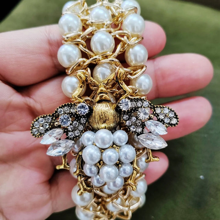 Decorative brooch with pearls and gold details held in a hand against a green background