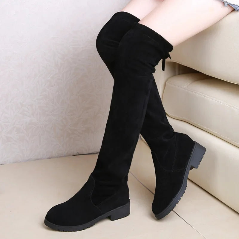 Black knee-high boots worn by a person sitting on a beige couch.