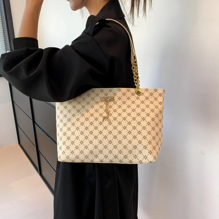 Women’s leather tote bag in black monogram plaid with gold chain shoulder strap and charm.