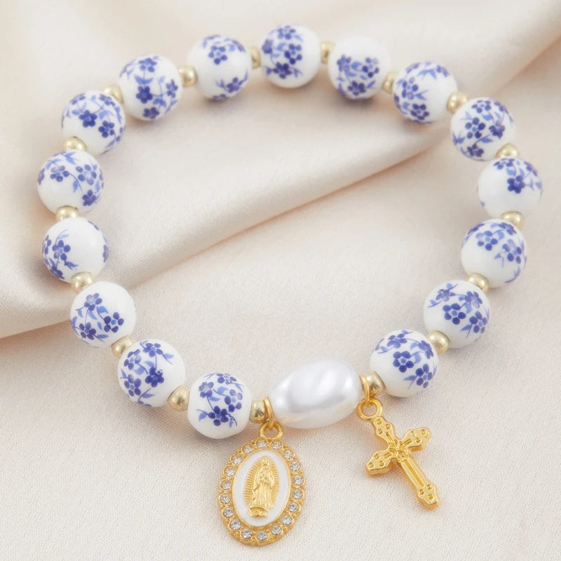 Bracelet with white beads featuring blue floral patterns, gold charms, and a cross on a beige background.