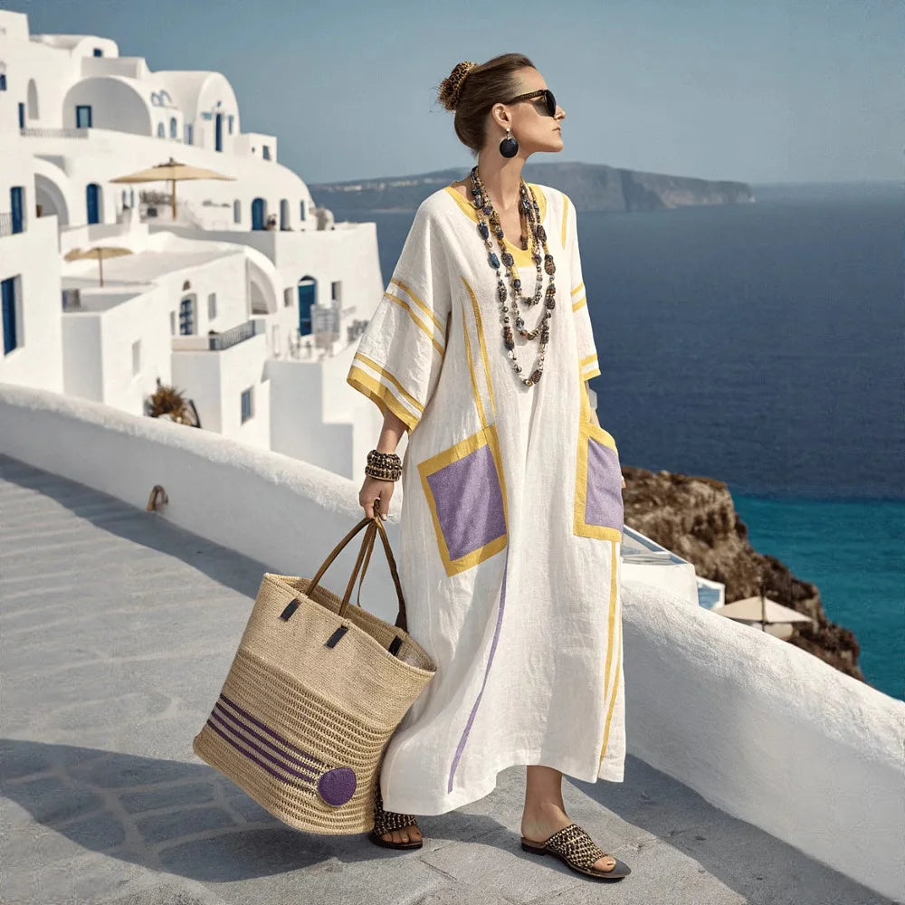 Woman in a white dress with purple accents standing on a Mediterranean cliffside path.