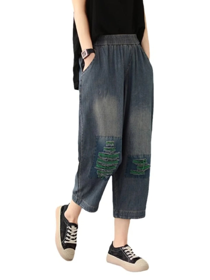 Person wearing denim capri pants with patches on a white background