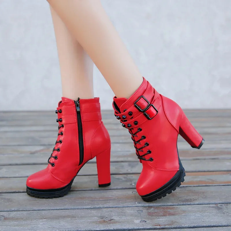 Red high-heeled boots with black buckles and laces on a wooden floor.
