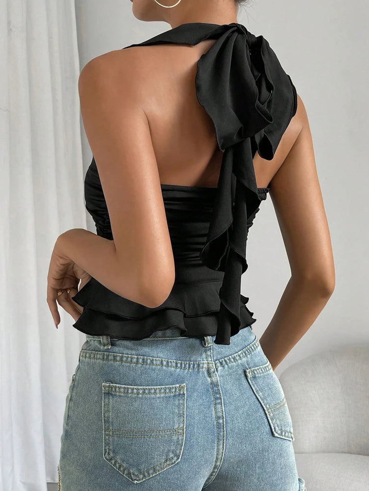 Person wearing a black ruffled top and blue jeans against a neutral background