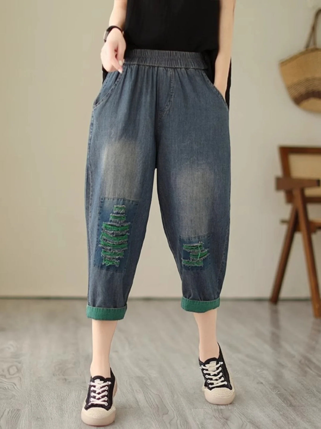 Person wearing blue denim capri pants with patches indoors.