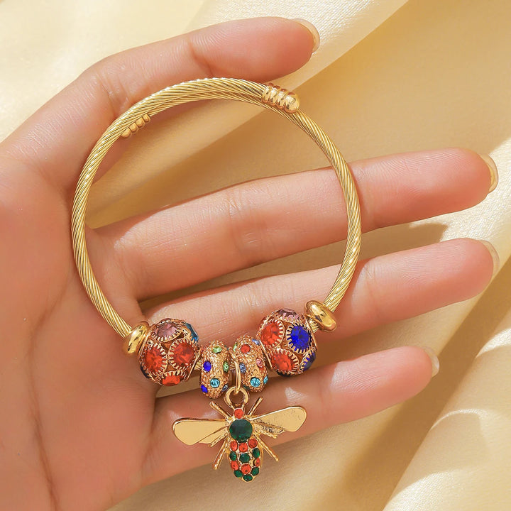 Goldfarbener Armreif mit bunten Perlen, runden Strass-Details und Flügel-Anhänger