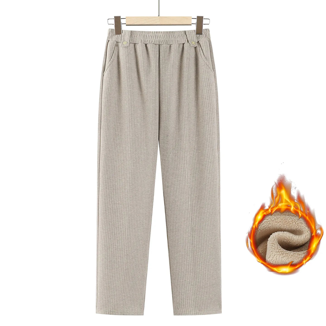 A pair of light beige ribbed knit pants with an elastic waistband, hanging on a wooden hanger against a white background, with a flame-and-shearling inset graphic on the right indicating warm lining.