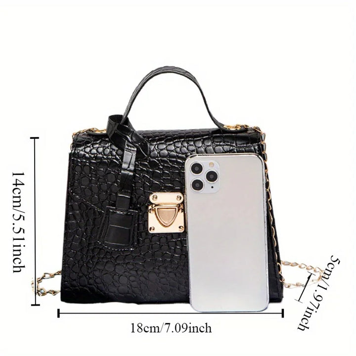 Black textured handbag with gold accents and a phone for scale on a white background