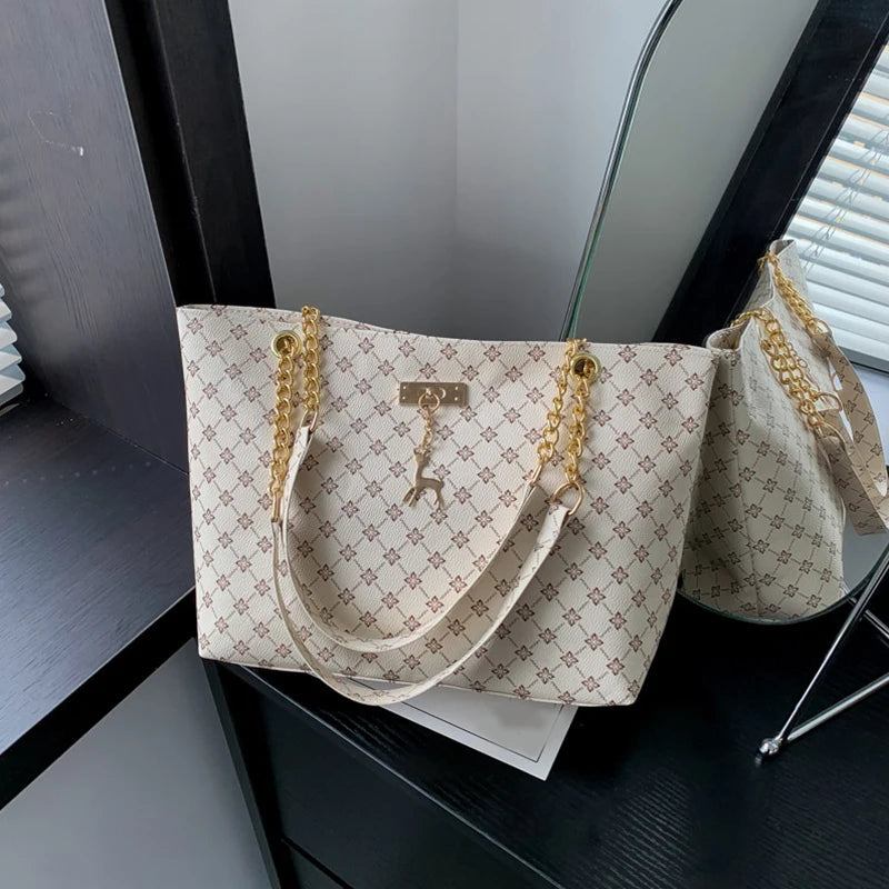 Women’s leather tote bag with light monogram plaid texture, gold chain handles, hanging charms.