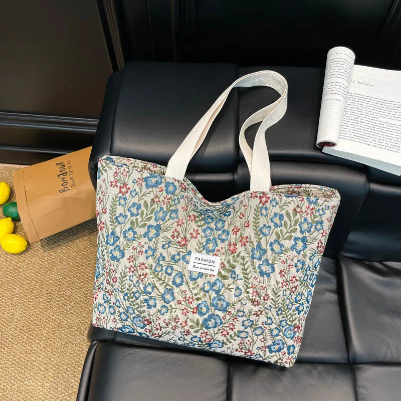 Canvas tote bag with blue floral and red accents, light handles, front label