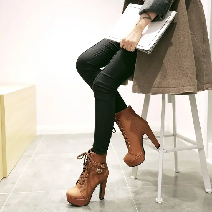 Person wearing brown high-heeled boots and black pants sitting on a white stool.