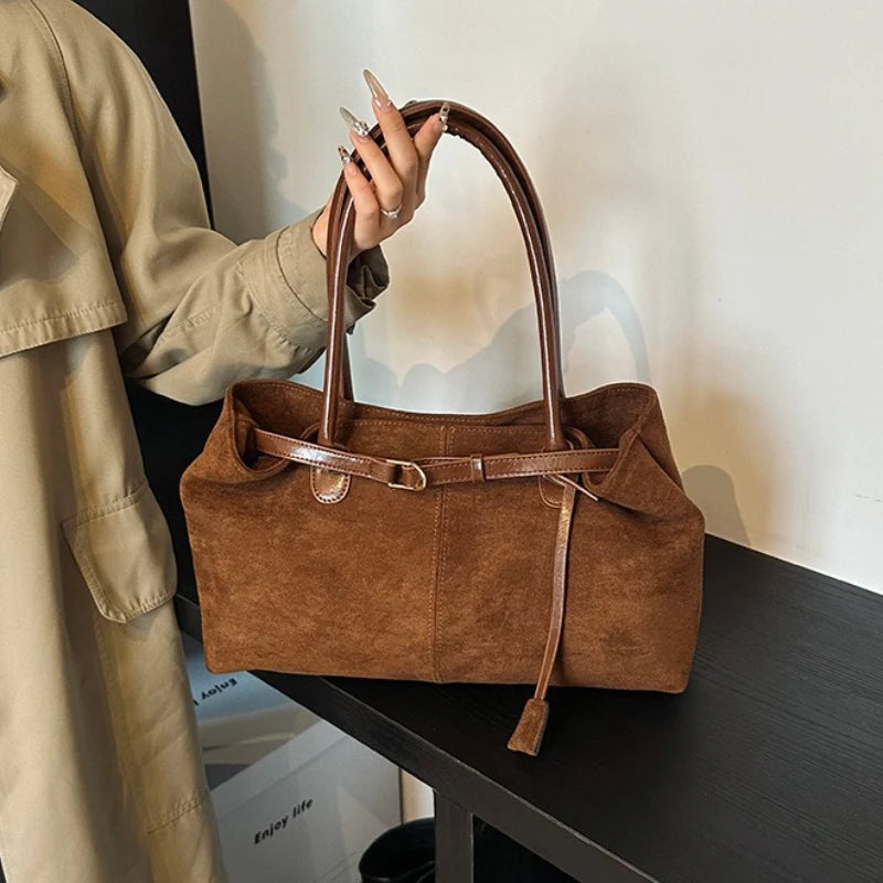 Women’s suede tote bag in brown with top handle and buckle strap detail.