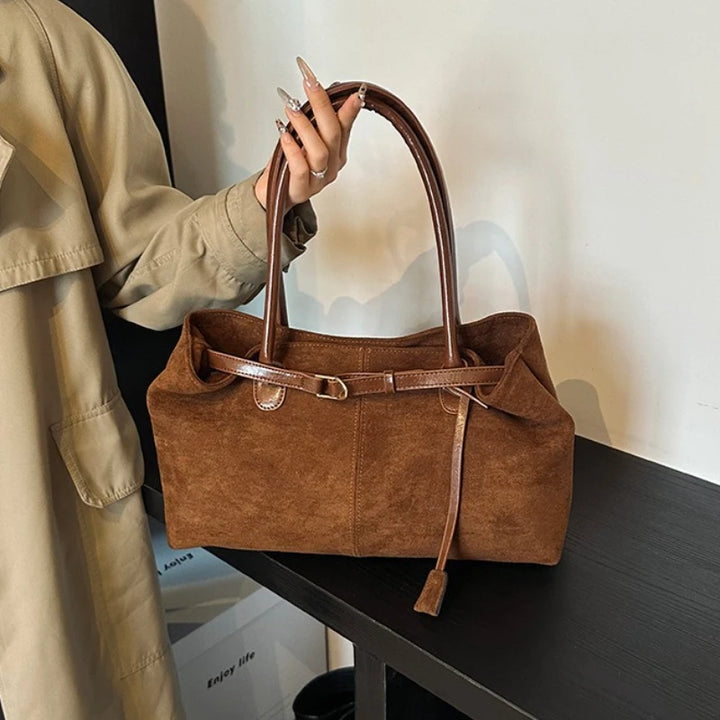 Women’s suede tote bag in brown with top handle and buckle strap detail.