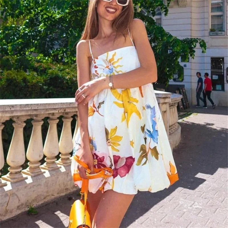 Woman in a floral dress standing outdoors with a building and greenery in the background