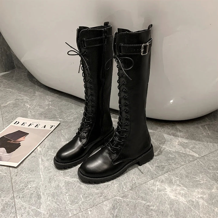 Black knee-high boots with laces on a gray tiled floor.