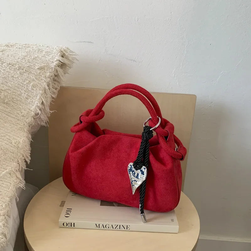 Red suede mini hobo crossbody bag with short handles, braided cord, and heart charm.