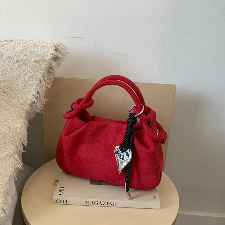 Red suede mini hobo crossbody bag with short handles, braided cord, and heart charm.