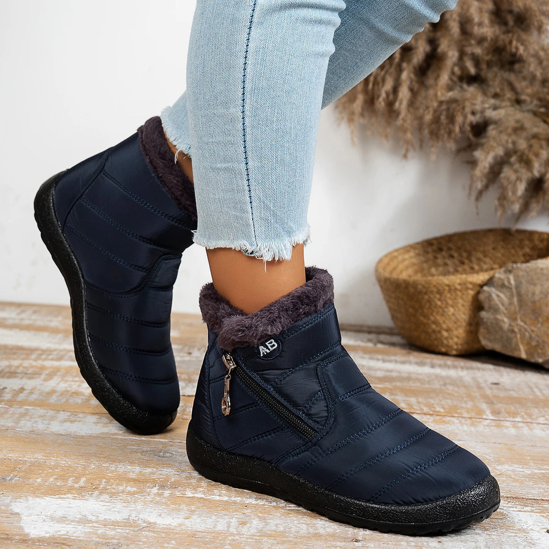 Person wearing navy blue winter boots with fur trim on a wooden floor.