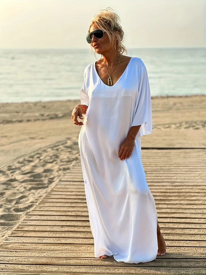 Woman in a white dress standing on a wooden boardwalk by the beach.