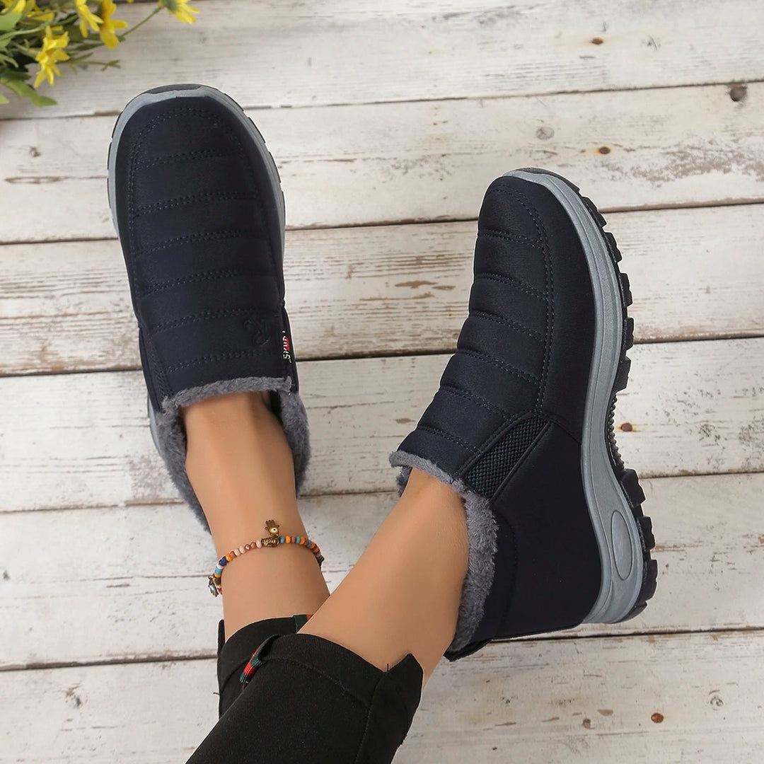 Black winter boots with gray fur lining worn by a person on a wooden floor.