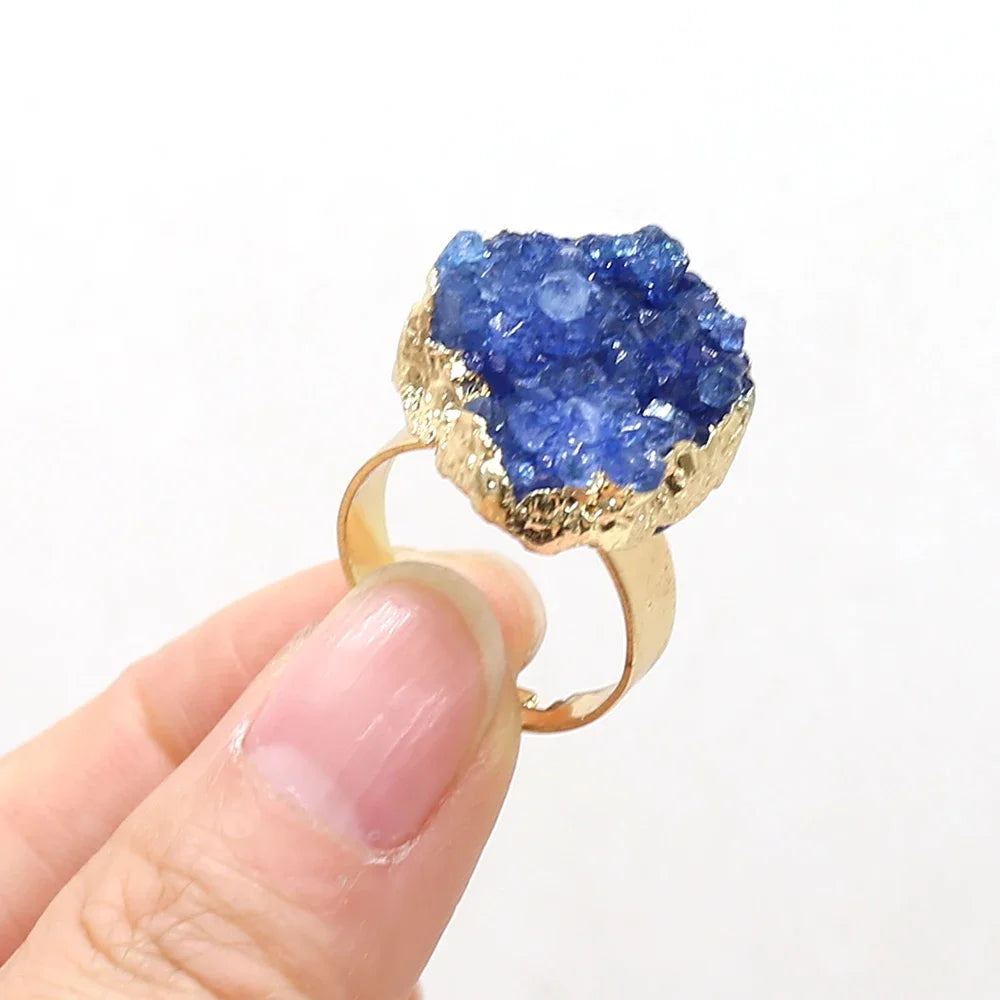 Gold ring with a blue gemstone held by a hand against a white background