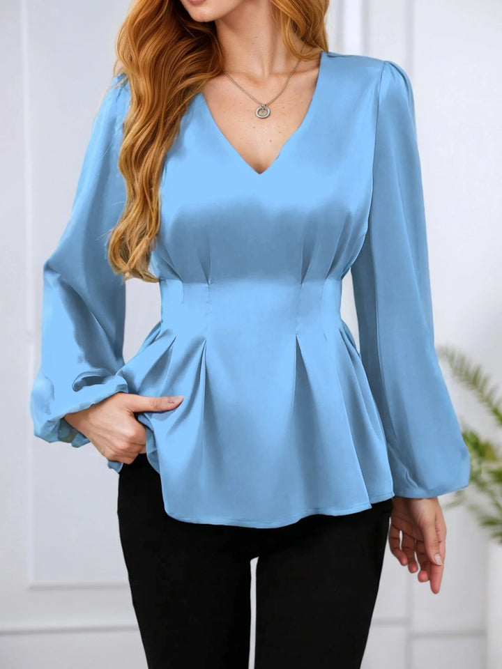Woman wearing a light blue peplum top with long sleeves against a white background