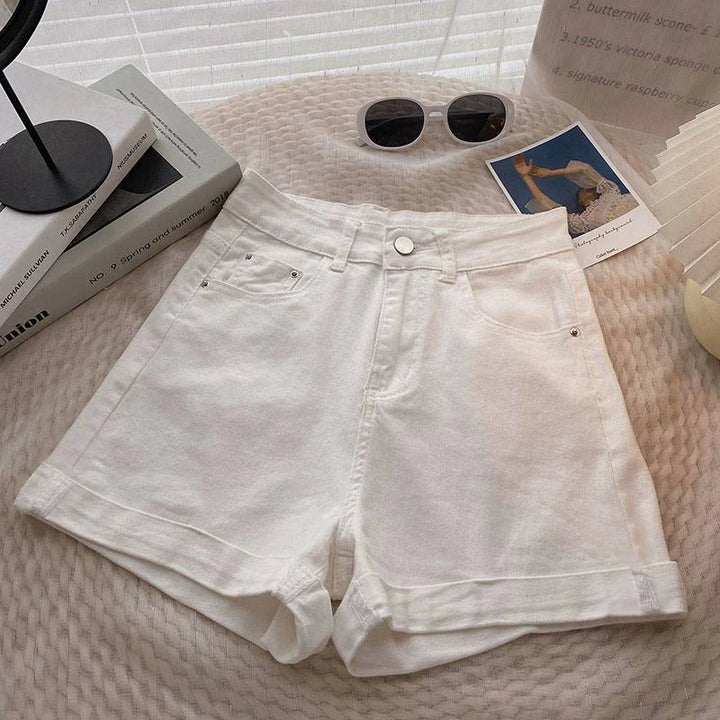 White denim shorts on a textured surface with books and sunglasses.