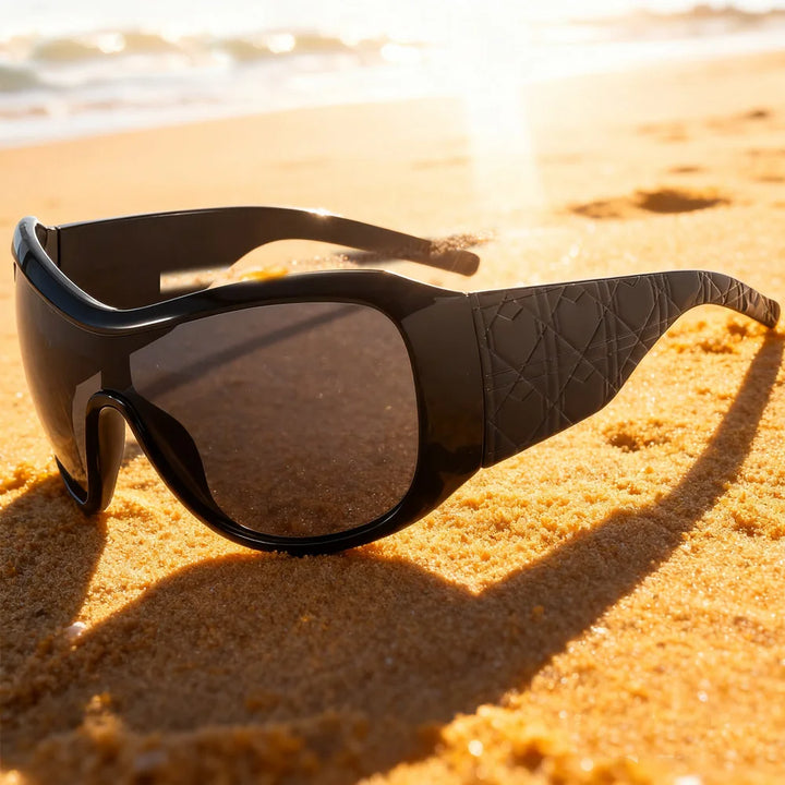 Black sunglasses on a sandy beach with ocean in the background