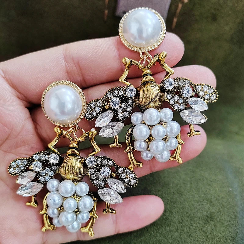 Pair of ornate earrings with pearls and gemstones held in a hand against a green background.