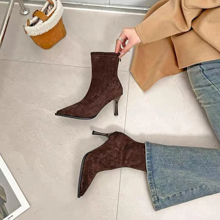 Brown suede pointed-toe ankle boots with slim stiletto heels, one shoe held
