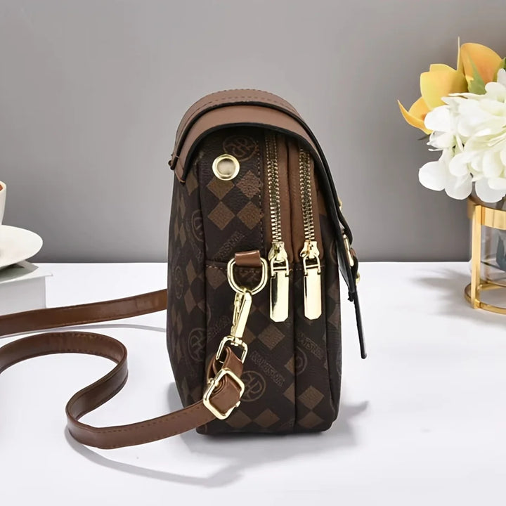 Brown patterned handbag with gold accents on a white surface with a gray background
